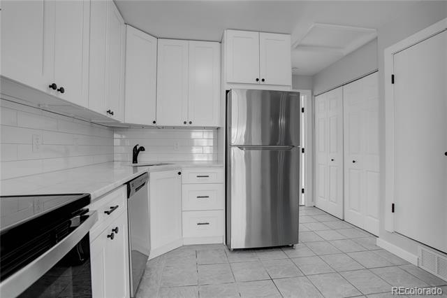 Vacant kitchen with white cabinets, subway tile backsplash, and stainless steel refrigerator.
