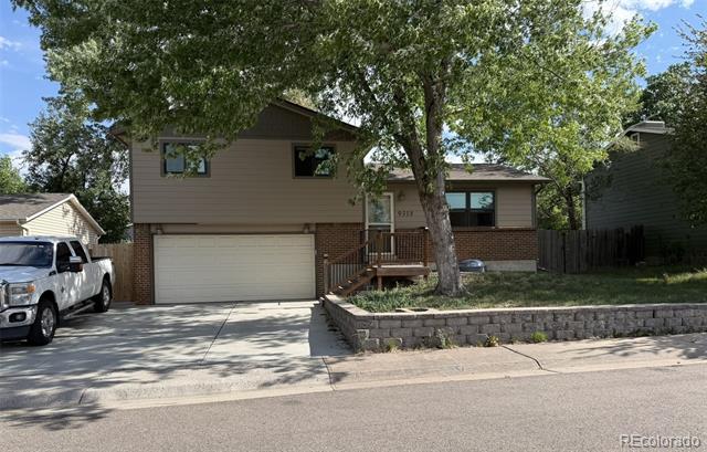 Two-story house with an attached garage, wide driveway, front porch, and large shade tree.
