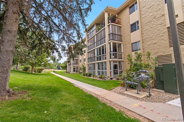 Multi-story tan condominium building with screened balconies beside a lawn and walkway.