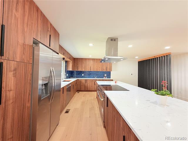 Modern kitchen with warm wood cabinets, blue tile backsplash, and a large white island.