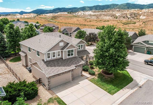 Aerial view of a two-story beige home with a double garage, corner lawn, and mountain foothills beyond.