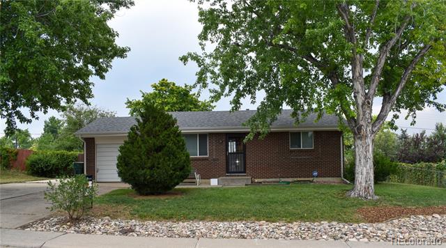 Single-story brick house with an attached garage, mature trees, and a stone border along the sidewalk.
