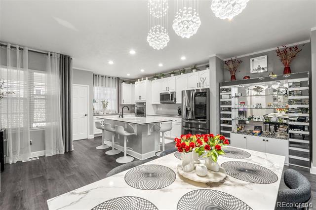 Open-plan kitchen and dining area with a large island, glass display shelves, and red flowers on the table.