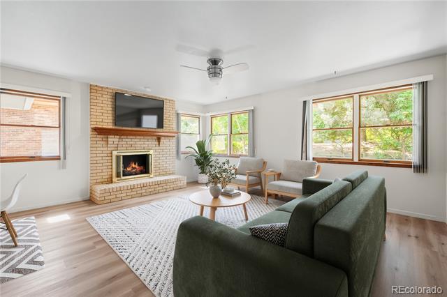 Living room with a green sectional, brick fireplace, and large windows overlooking trees.