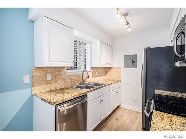 Galley kitchen with white cabinets, tan granite counters, tiled backsplash, and stainless steel dishwasher.