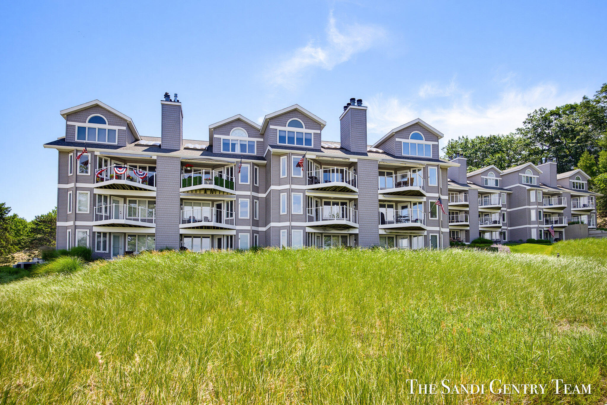 Gray condominium buildings with balconies behind a grassy dune.