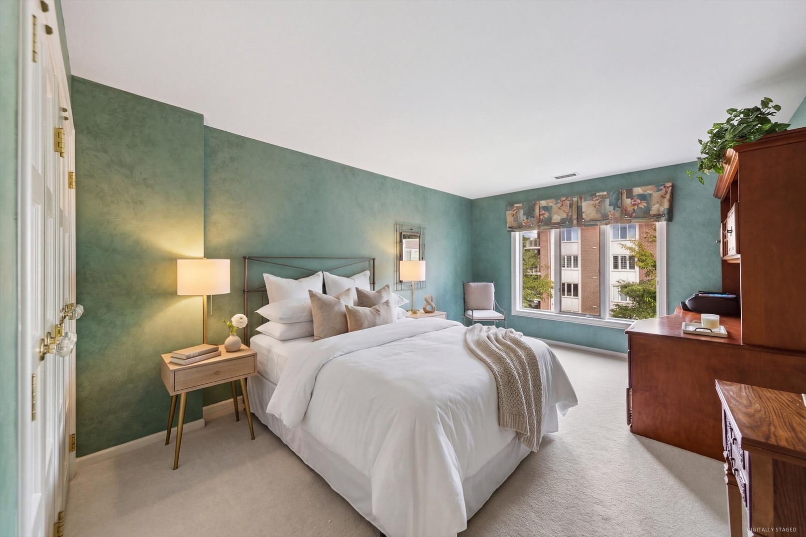 Staged bedroom with a white bed, teal-green walls, and a large window overlooking a neighboring building.