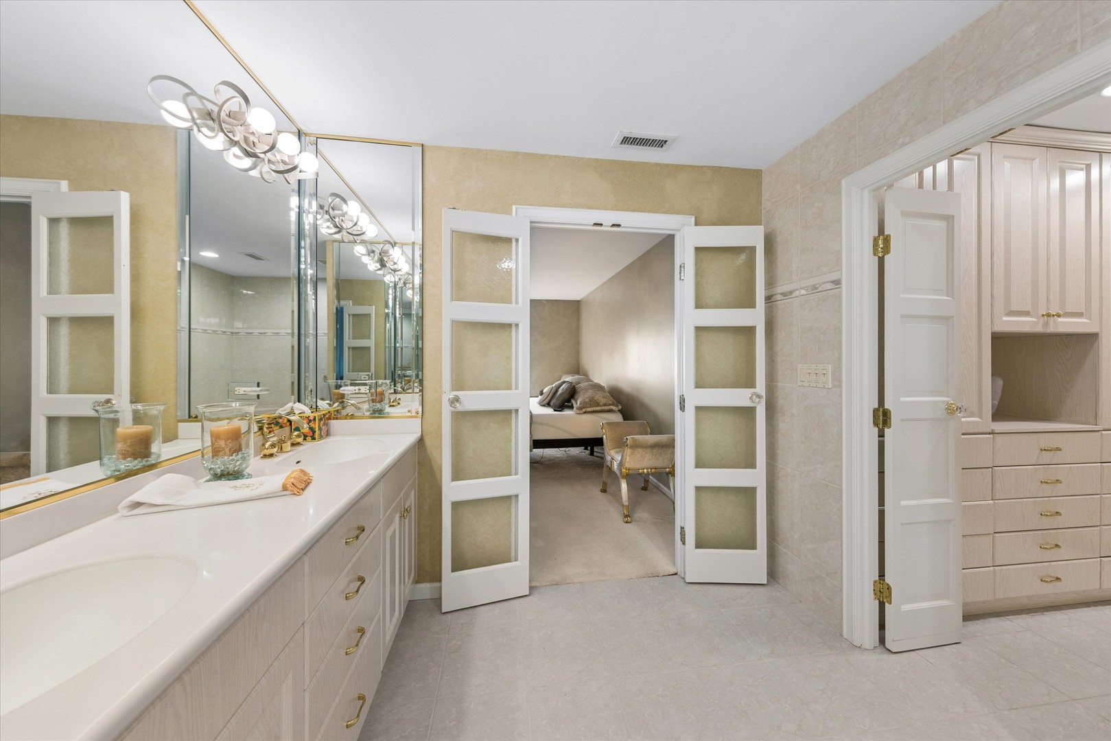 Bathroom with a long mirrored vanity, open doors to a bedroom, and built-in dressing cabinetry.