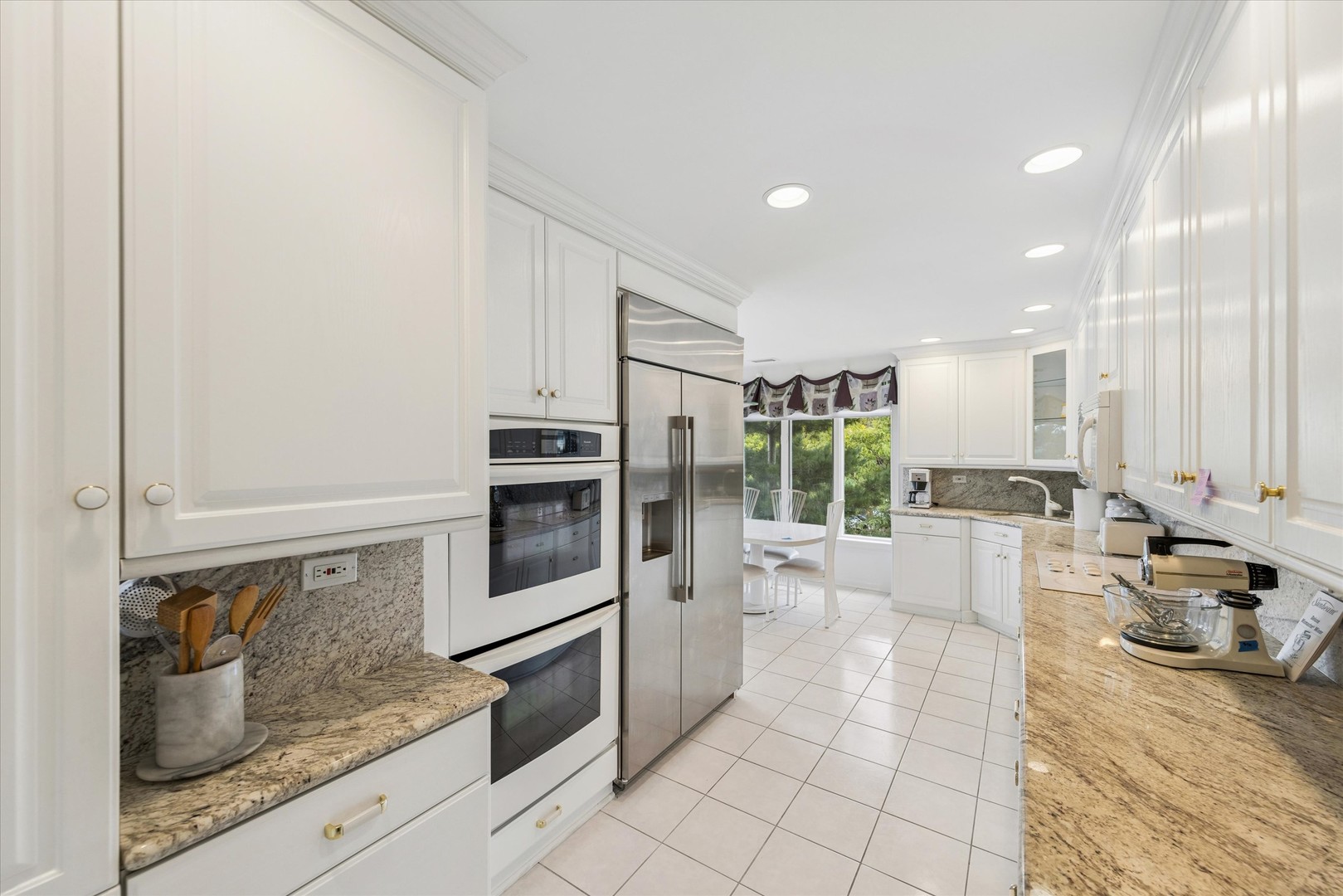 White kitchen with granite counters, stainless appliances, and a window-side dining nook.