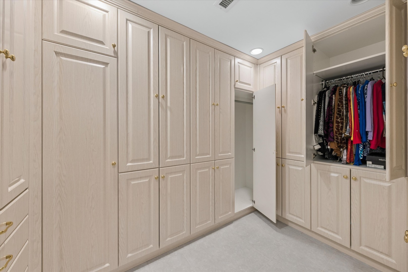 Walk-in dressing room with light wood cabinetry and colorful clothes hanging in an open closet.