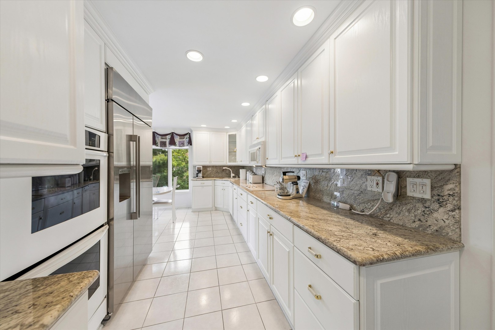 Galley kitchen with white cabinets, granite counters, stainless steel appliances, and a window overlooking greenery.