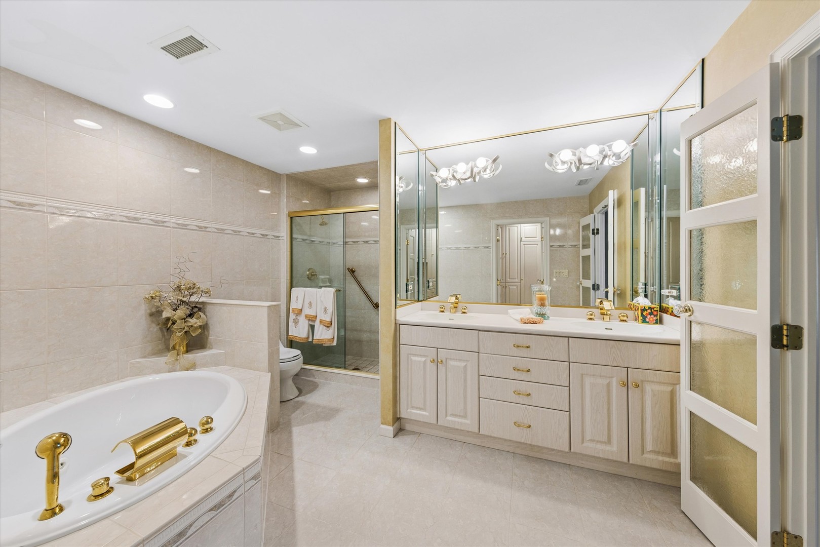 Tiled bathroom with a soaking tub, glass shower, and long double-sink vanity.