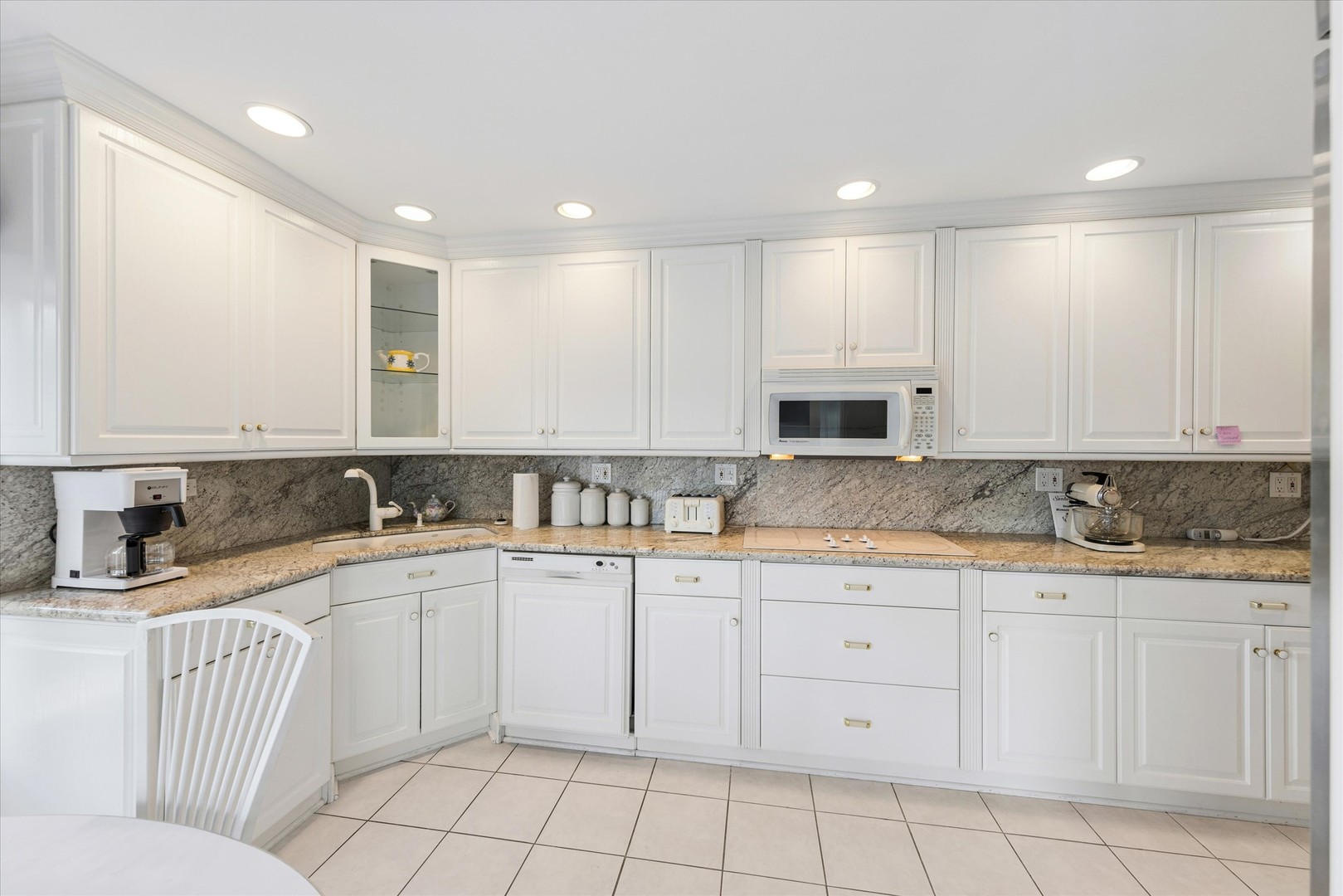 Kitchen with white cabinets, granite counters and backsplash, and a built-in microwave.