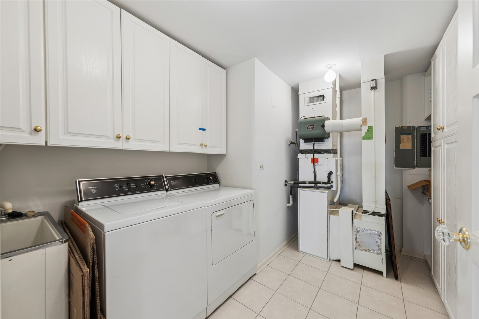 Laundry room with a washer and dryer, built-in cabinets, utility sink, and mechanical equipment.