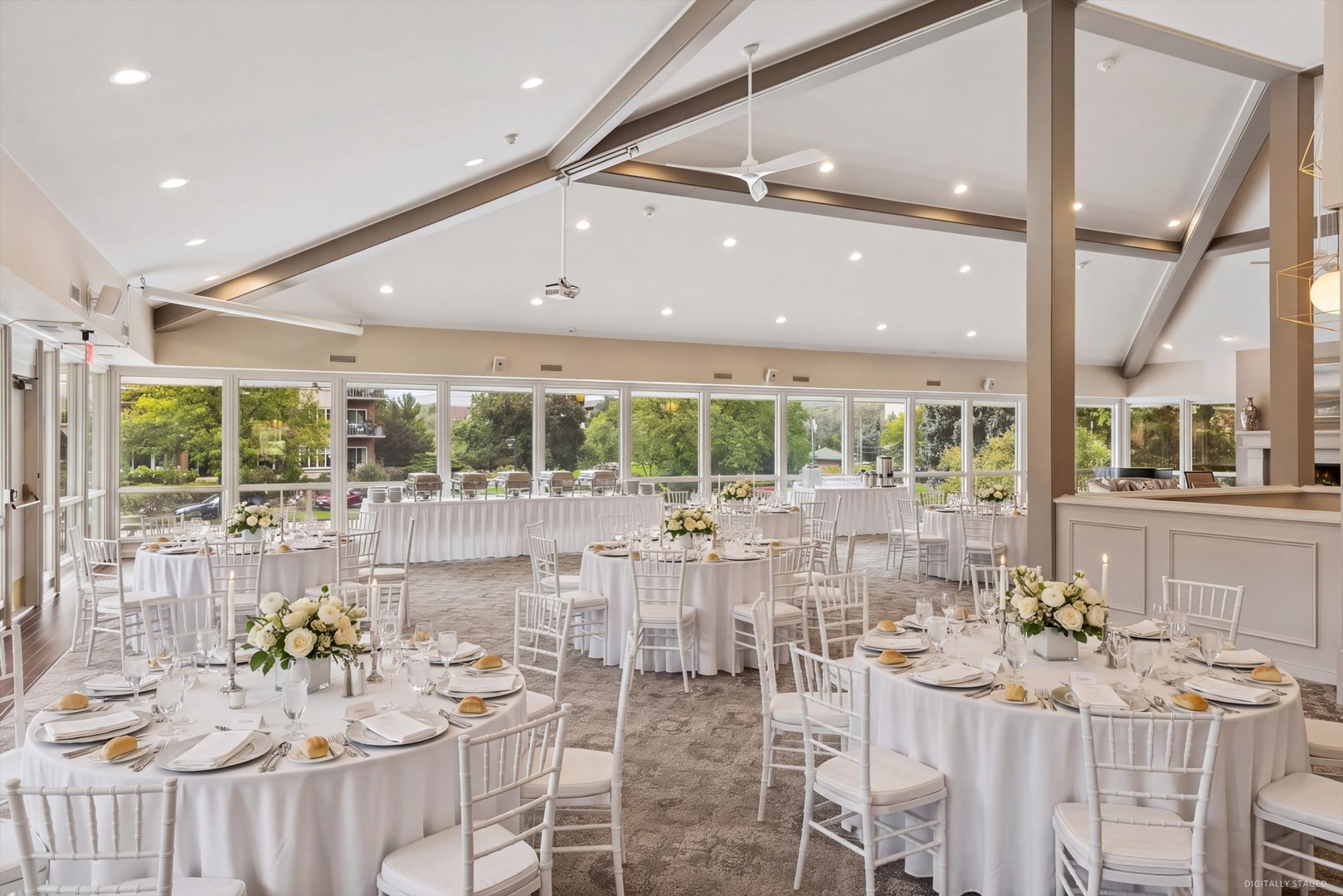 Community event room set for a banquet, with tall windows, a beamed ceiling, and round tables.