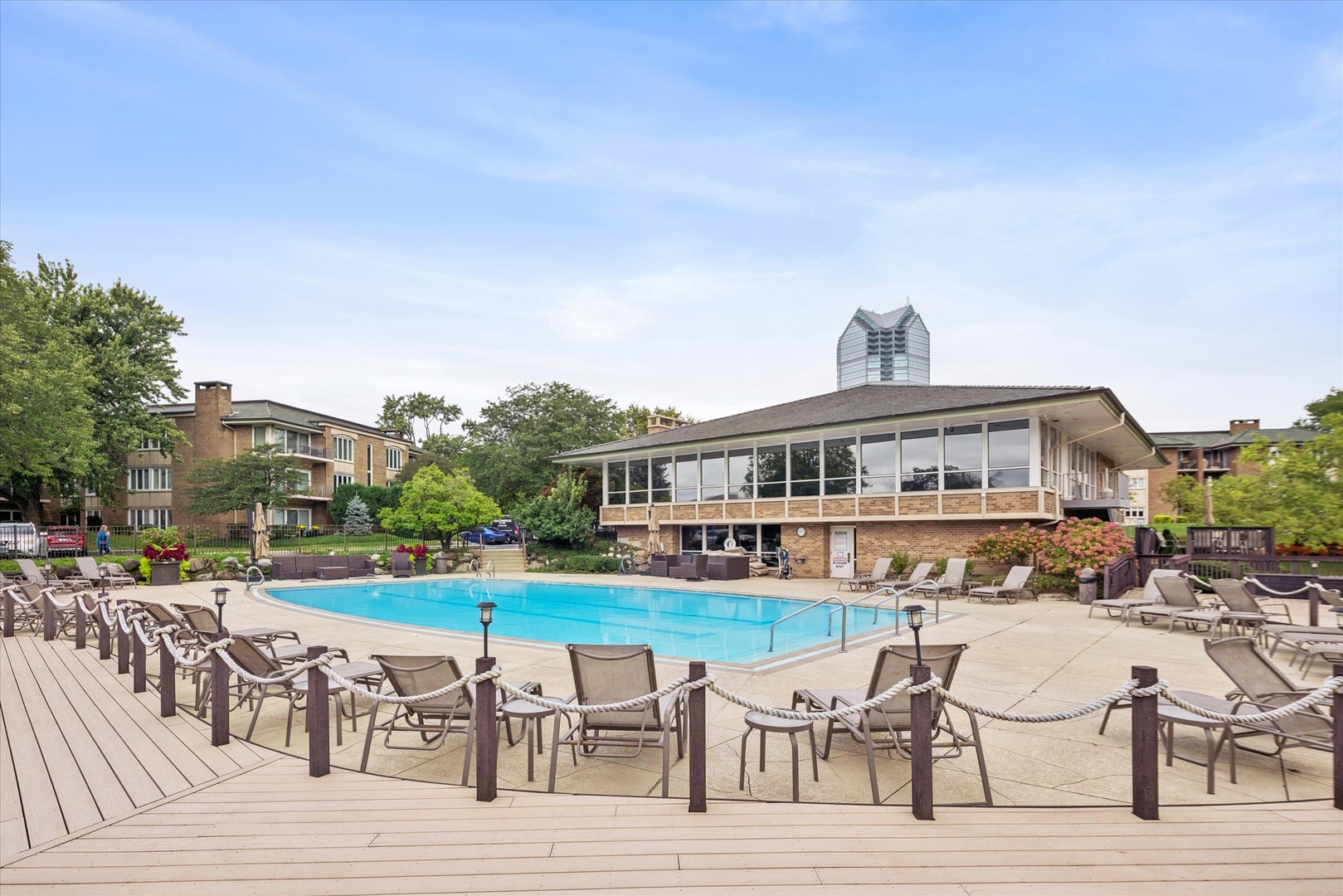 Outdoor pool and lounge deck beside a glass-fronted clubhouse and condominium buildings.