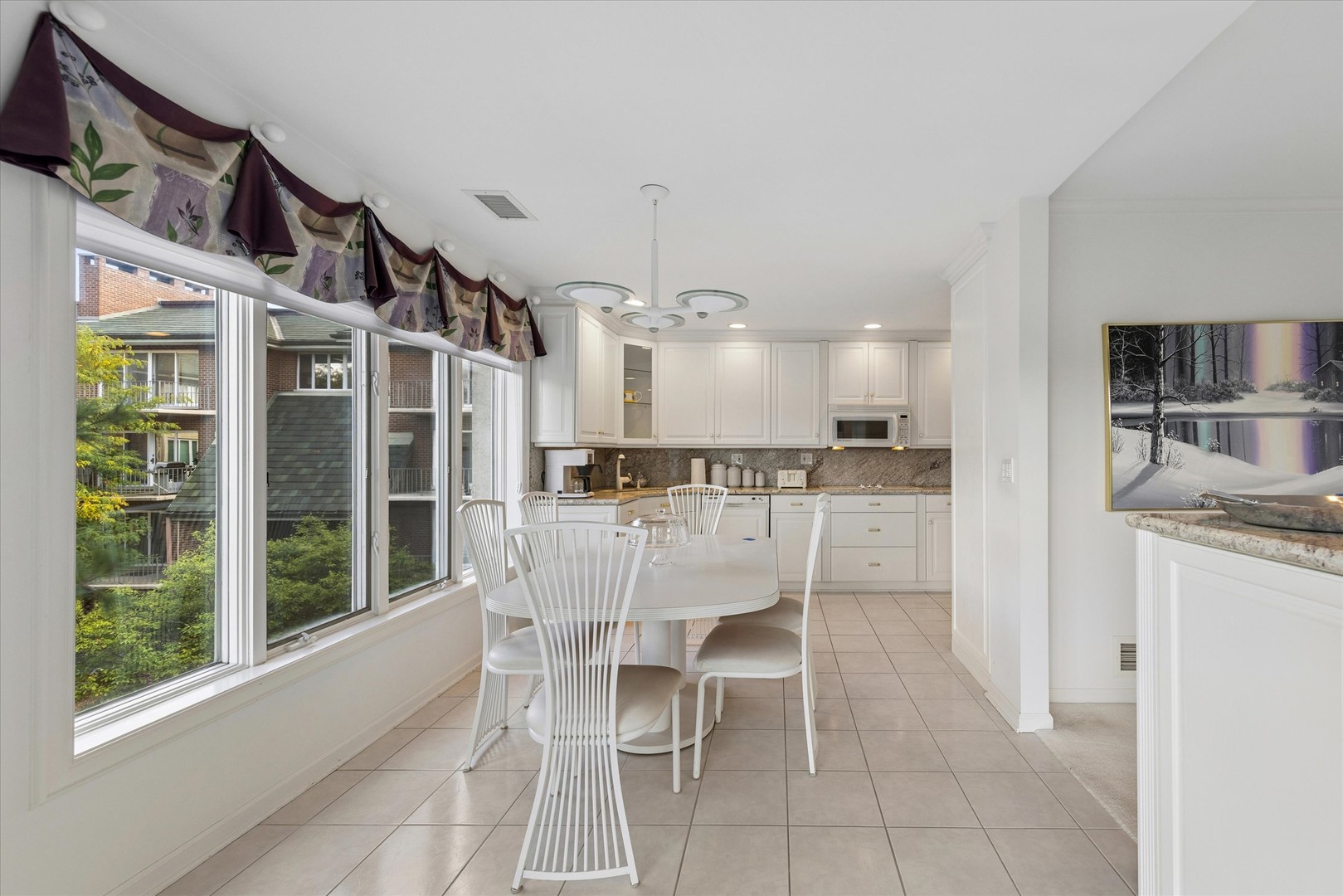 Kitchen and dining area with white cabinetry, an oval table, and large windows overlooking trees and neighboring homes.