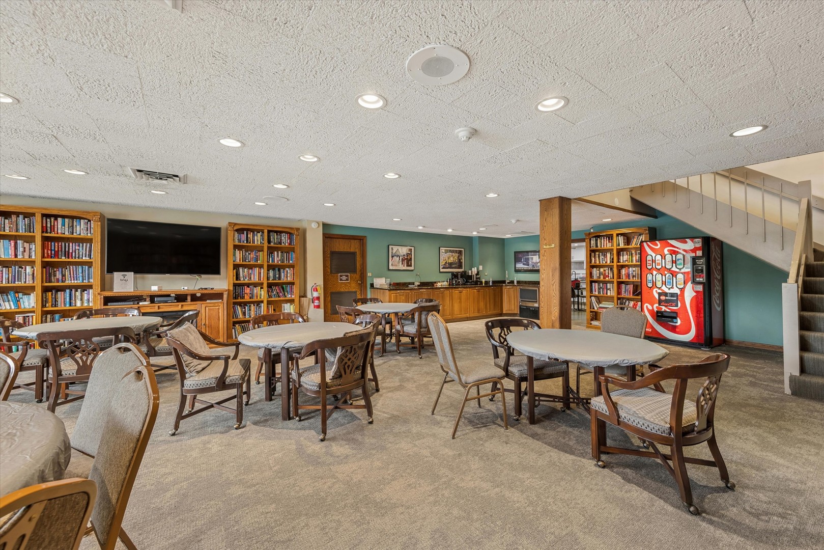 Club lounge with bookshelves, café tables, a television, coffee counter, and vending machine.