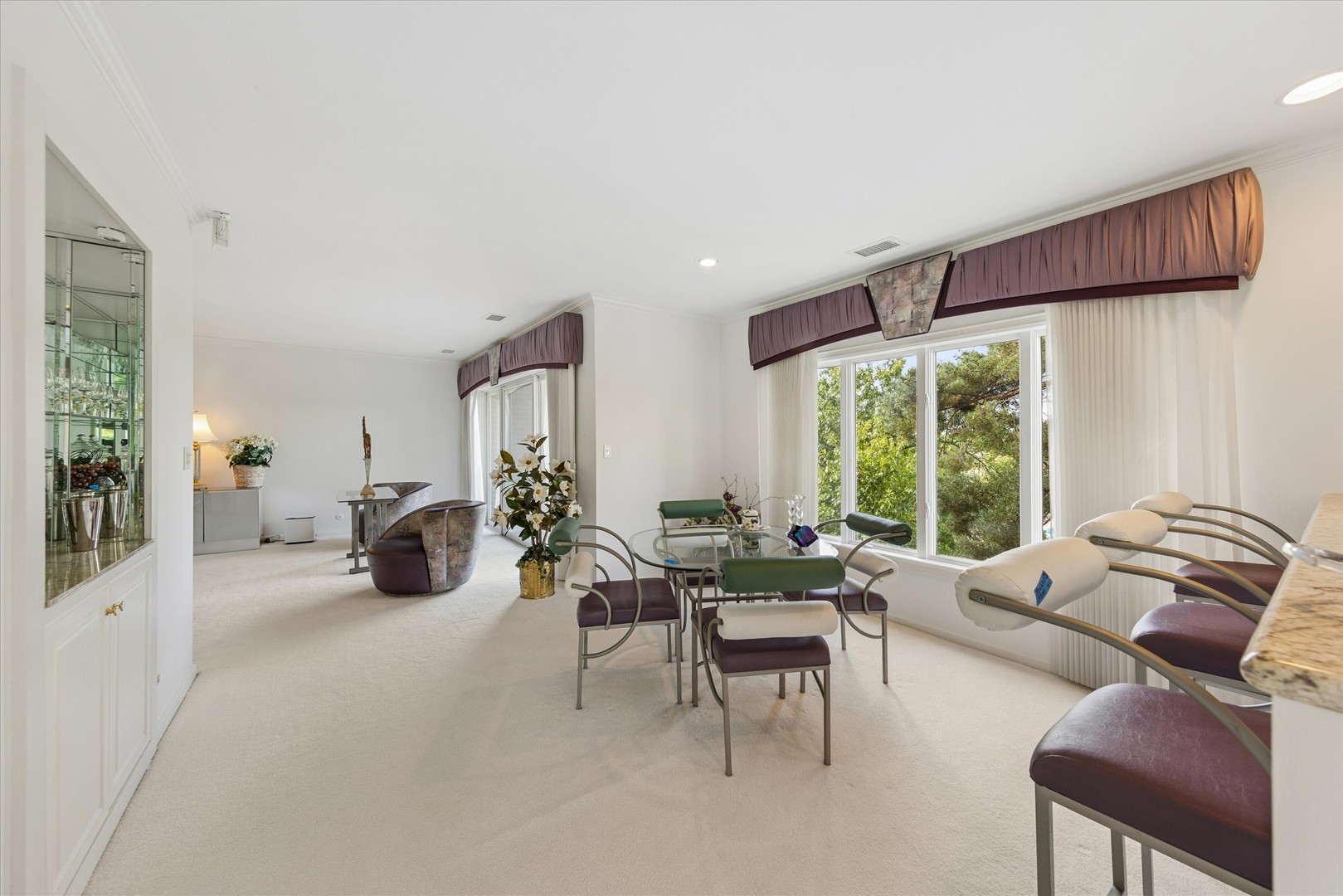 Furnished sitting area with curved chairs and large windows overlooking leafy trees.