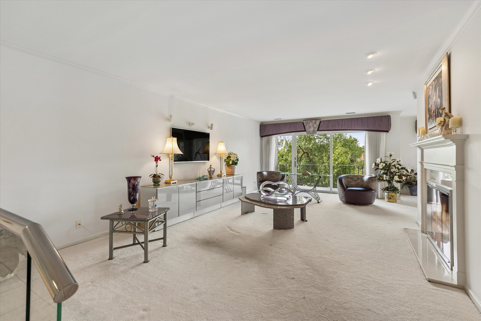 Living room with a white fireplace and sliding doors to a leafy balcony.