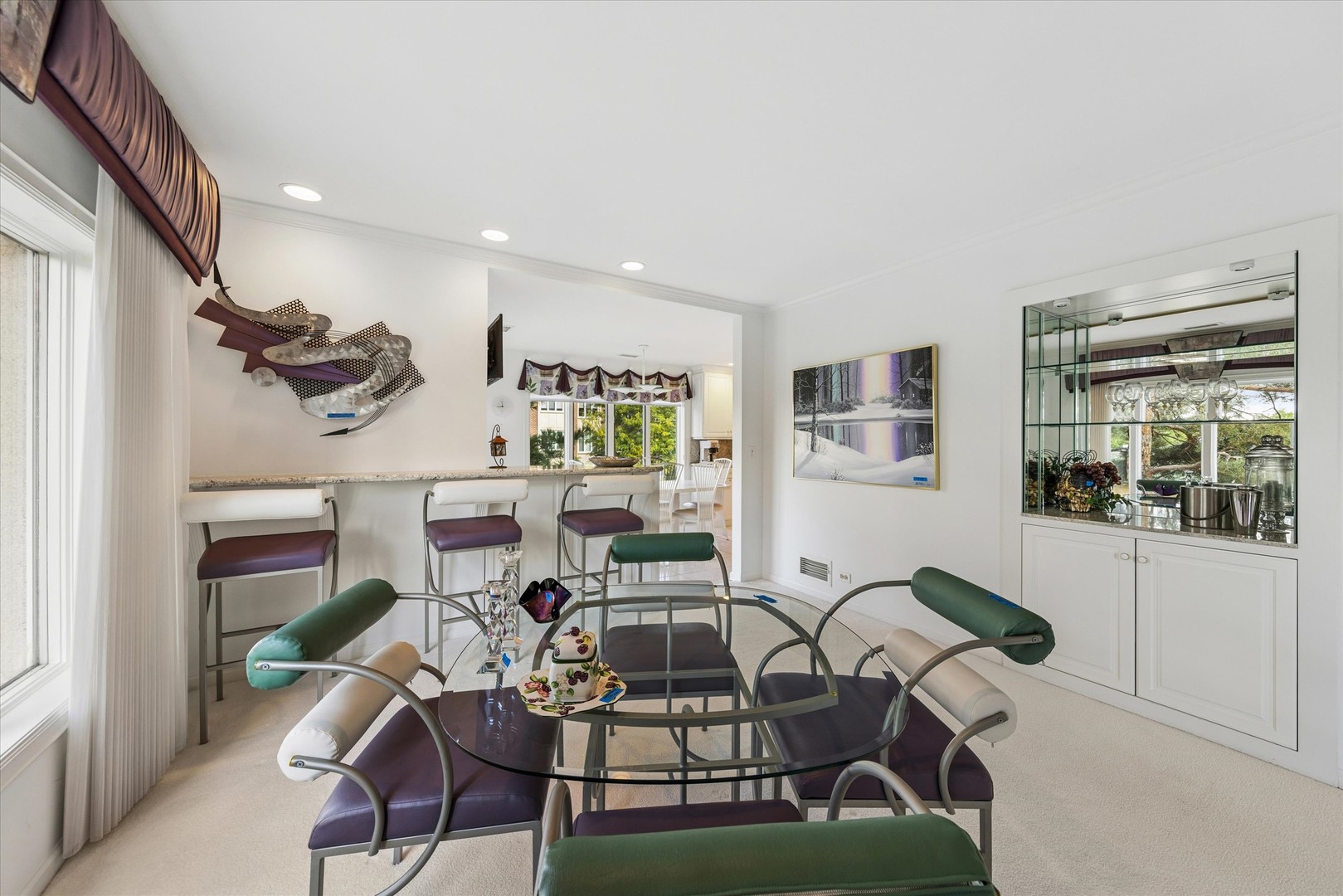 Dining room with a glass table, colorful chairs, and a breakfast bar opening to the kitchen.