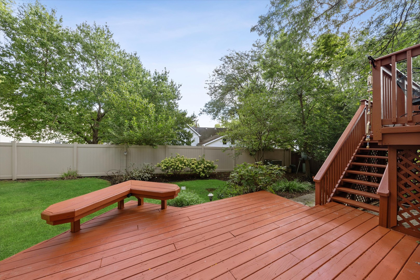 Backyard deck with built-in bench, stairs, lawn, mature trees, and fenced garden.