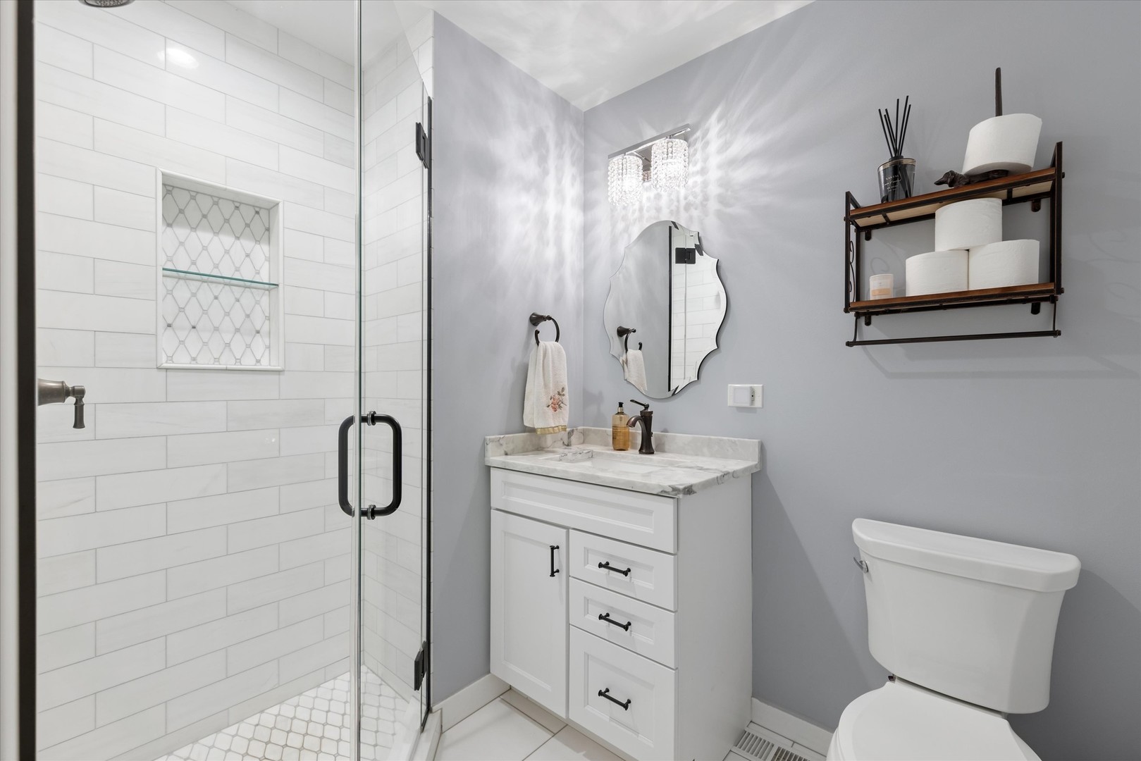 Bathroom with a glass shower, geometric tile niche, marble-topped vanity, and decorative mirror.