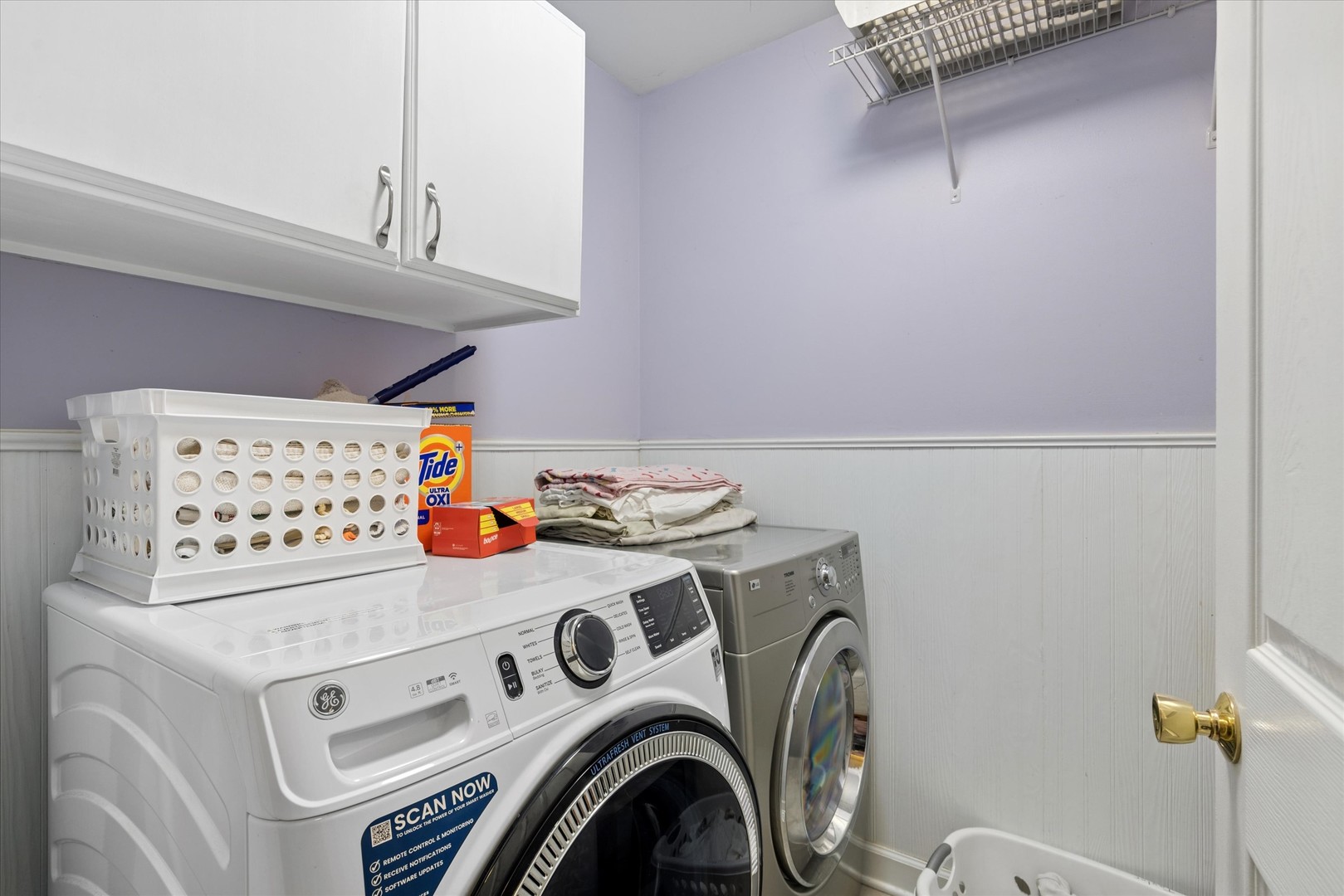 Laundry room with front-loading washer and dryer beneath overhead cabinets.