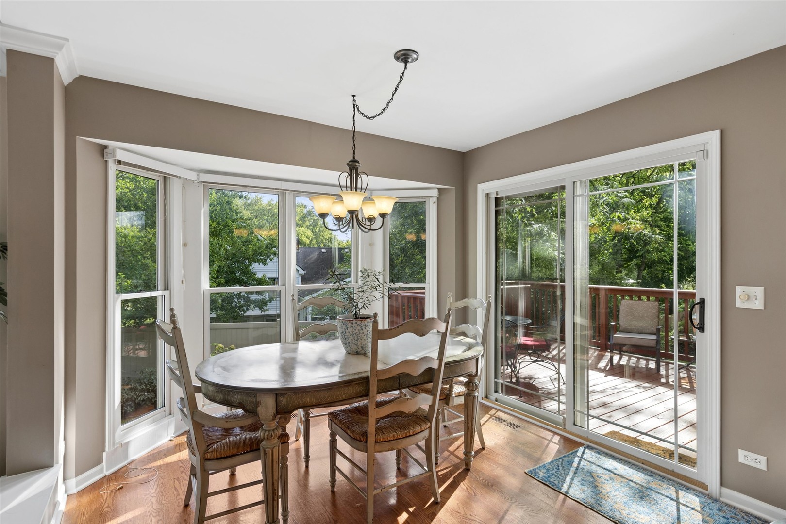 Dining room with bay windows, a chandelier, and sliding glass doors opening to a wooded deck.
