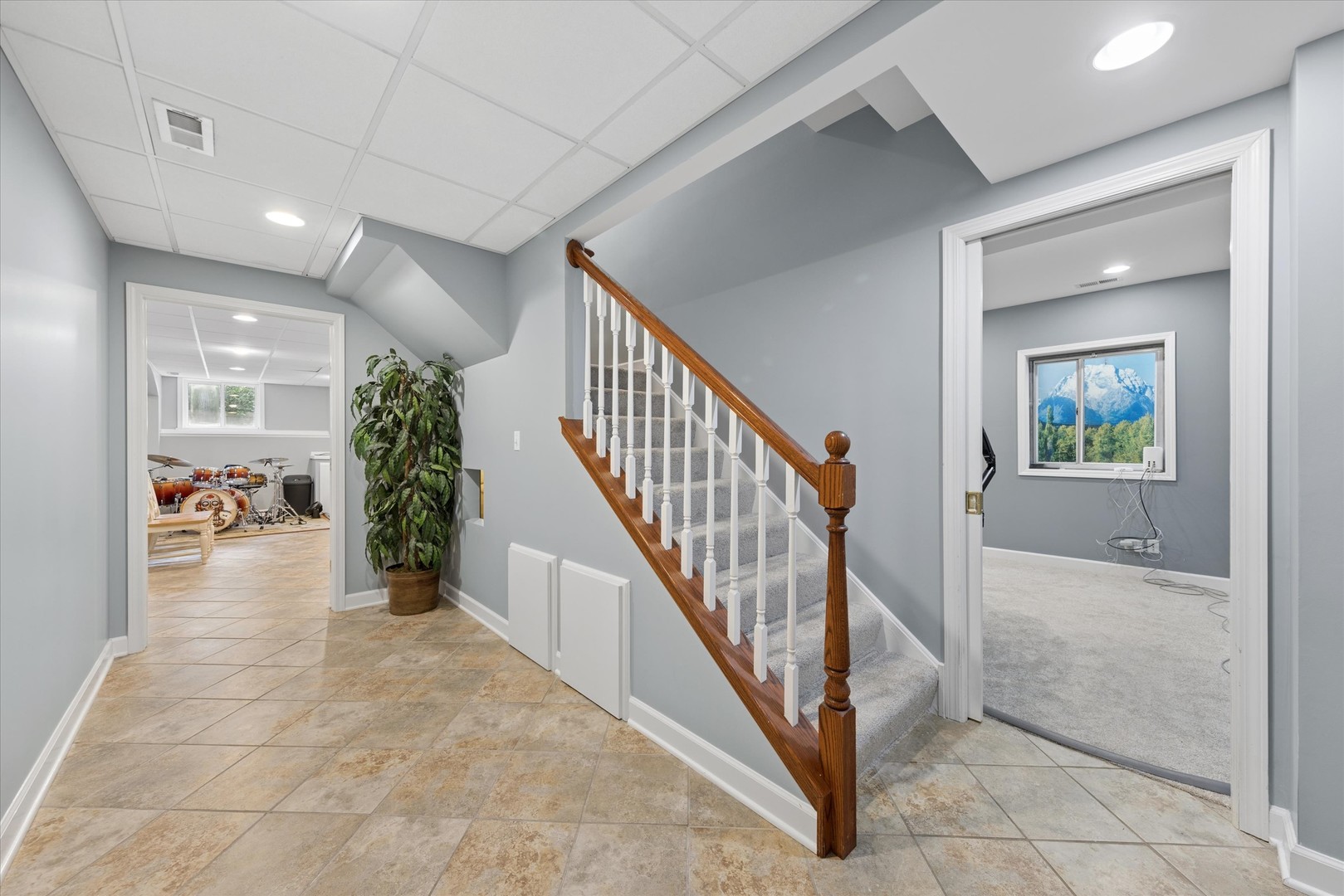 Tiled hallway with a carpeted staircase, wood handrail, and adjoining drum room.