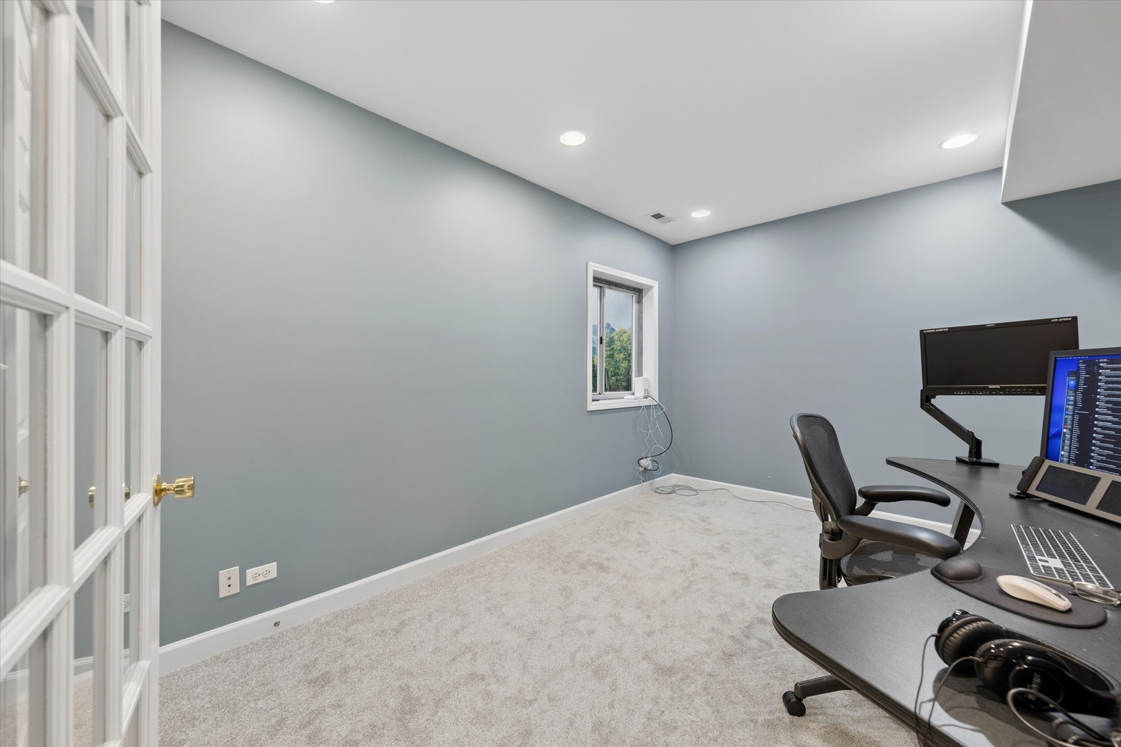 Home office with gray-blue walls, a carpeted floor, and a desk with multiple monitors.
