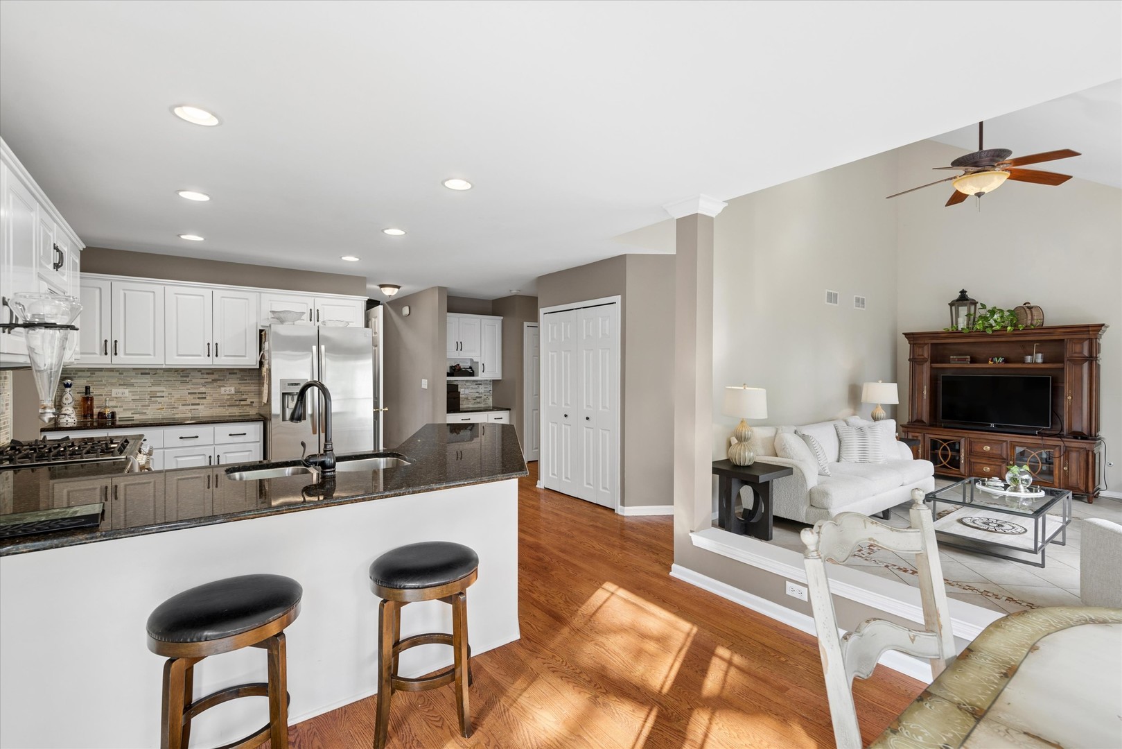 Open kitchen and living area with white cabinets, granite island, and hardwood floors.
