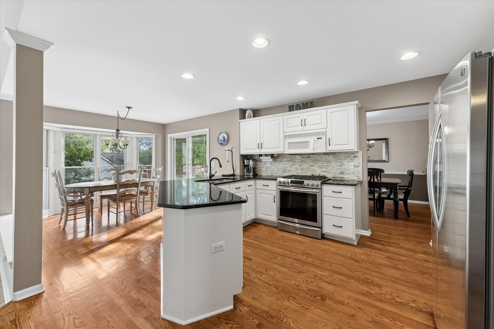 Kitchen with white cabinetry, black granite island, stainless steel appliances, and hardwood floors.