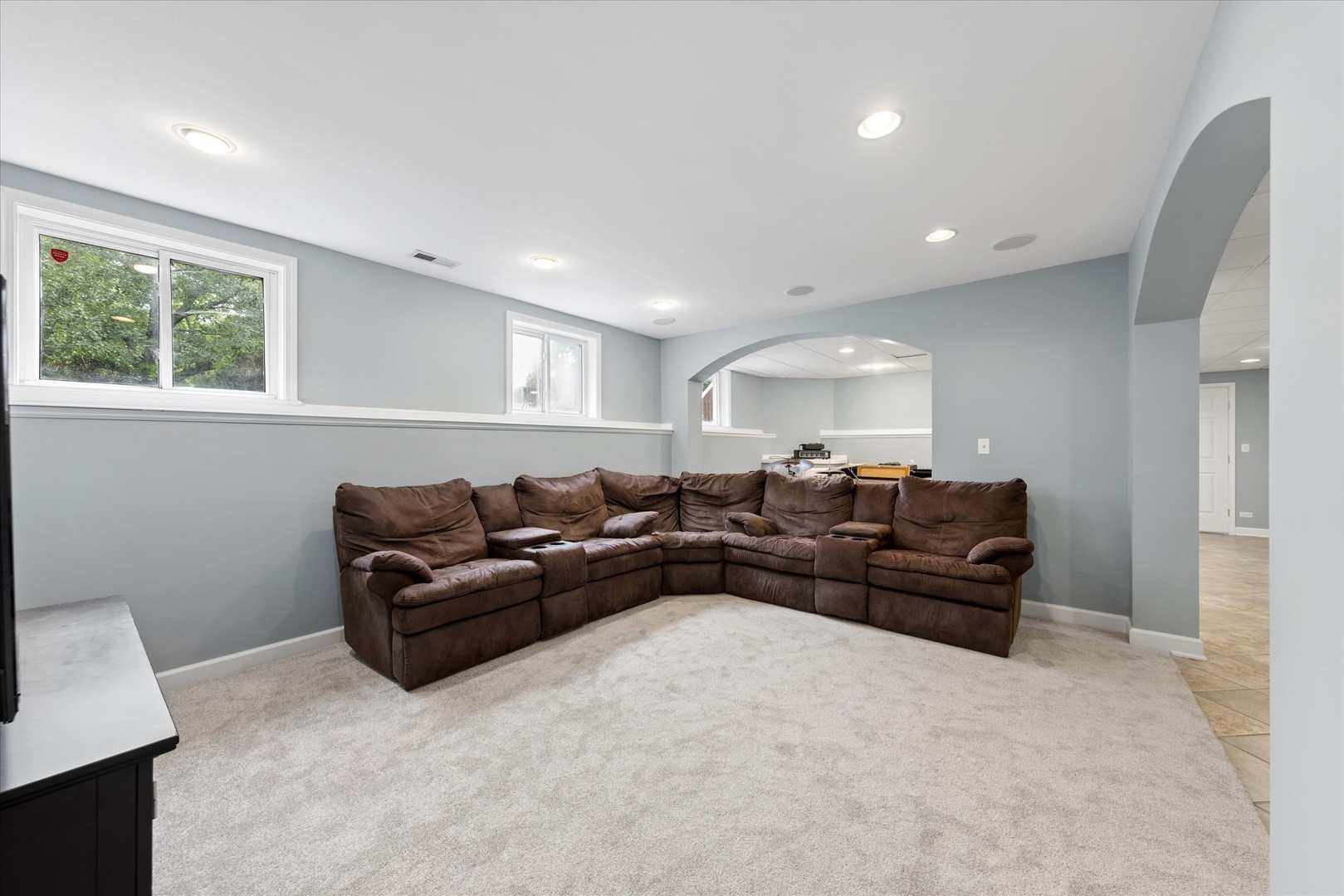 Recreation room with a brown sectional, light carpet, and arched openings.