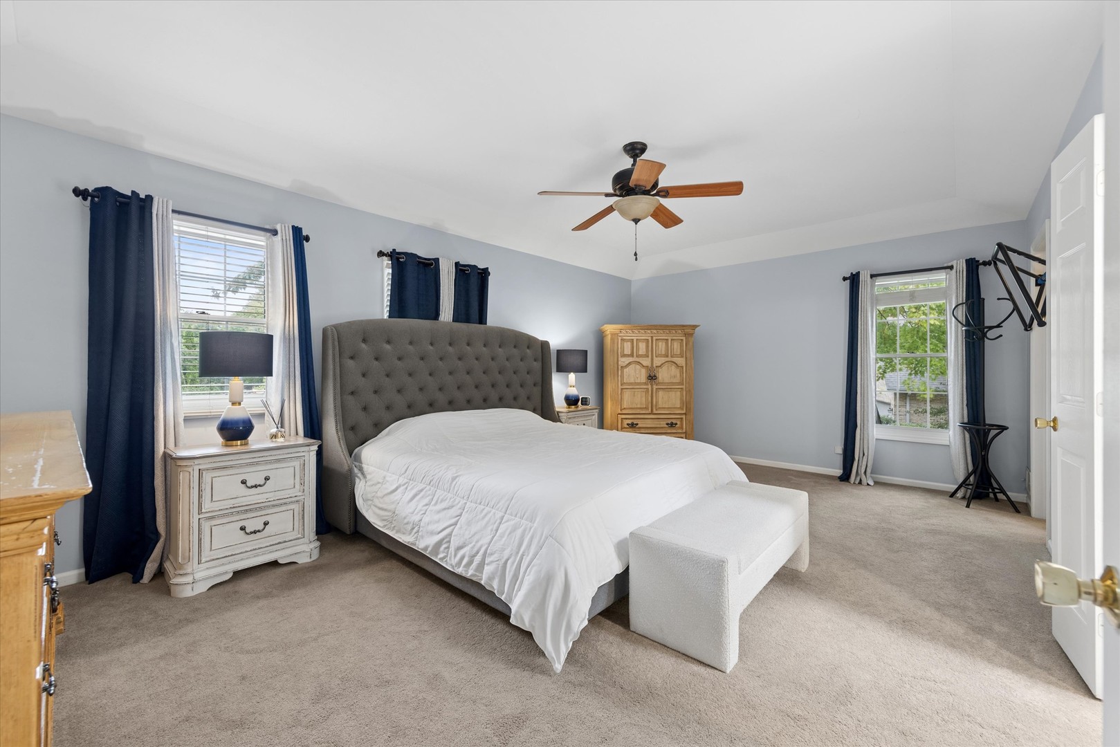 Furnished bedroom with a tall tufted headboard, vaulted ceiling, and navy curtains.