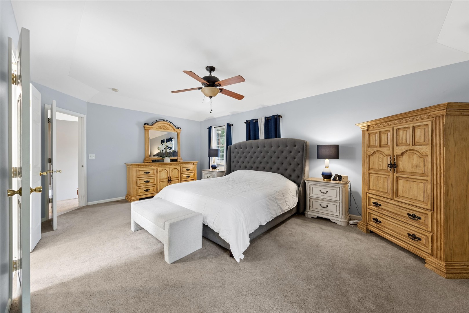 Furnished bedroom with a gray tufted bed, wooden furniture, and ceiling fan.