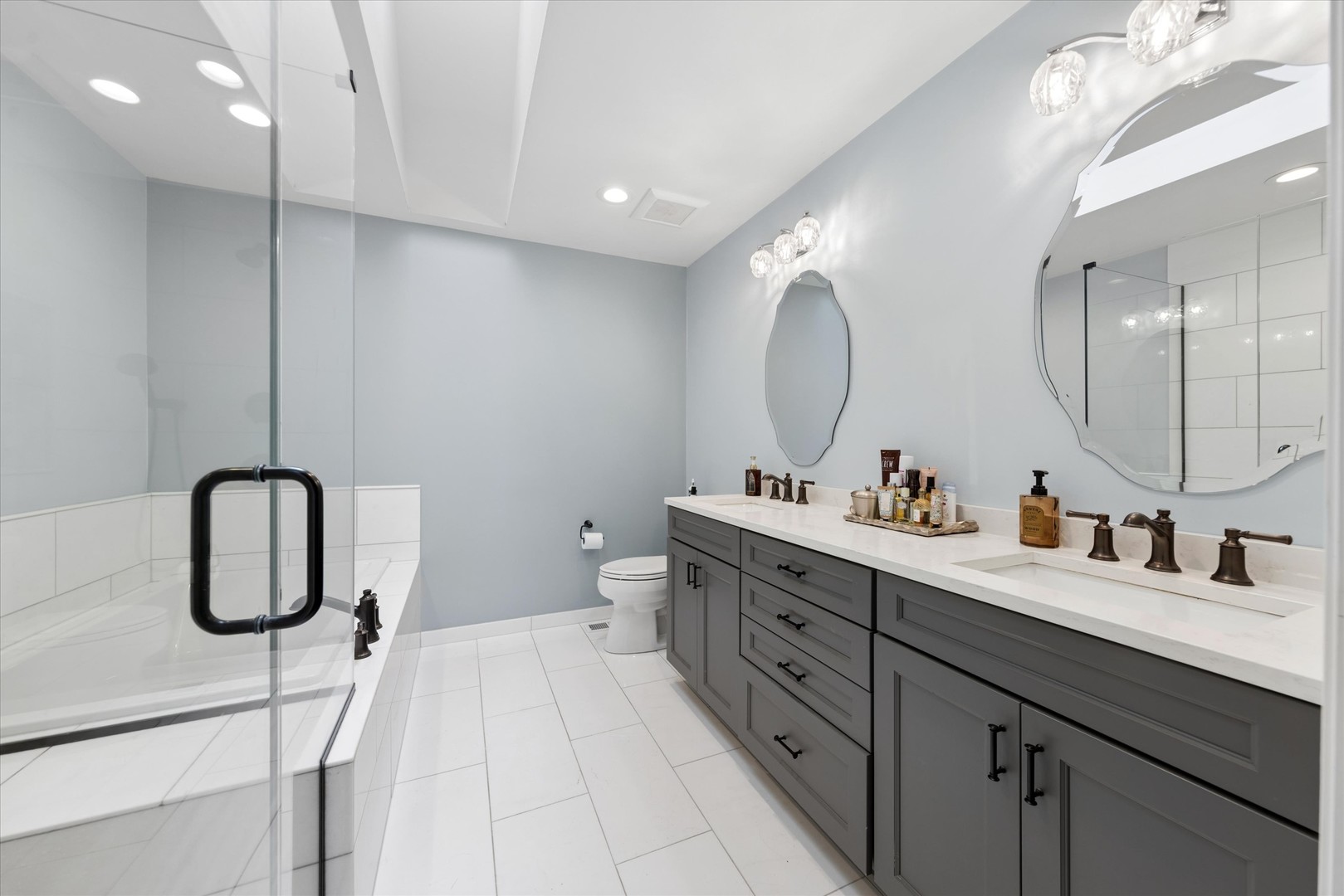 Modern bathroom with a long gray double vanity and glass-enclosed tiled shower.