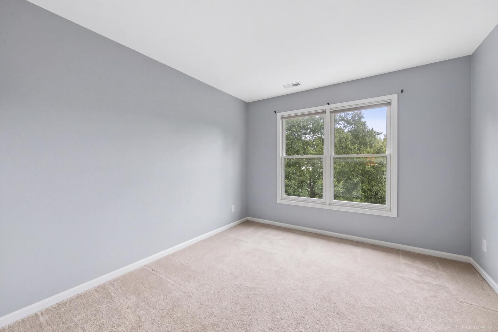 Empty carpeted bedroom with gray walls and a large double window overlooking trees.