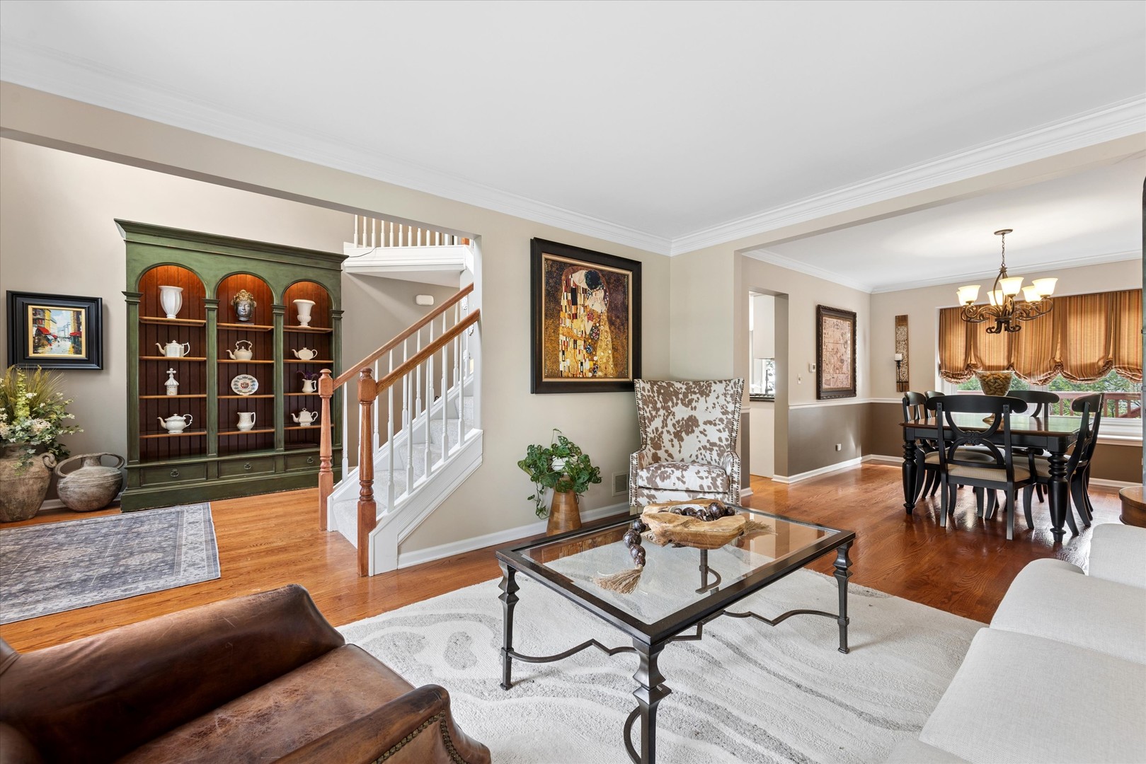 Living room with hardwood floors, glass coffee table, staircase, and dining area beyond.