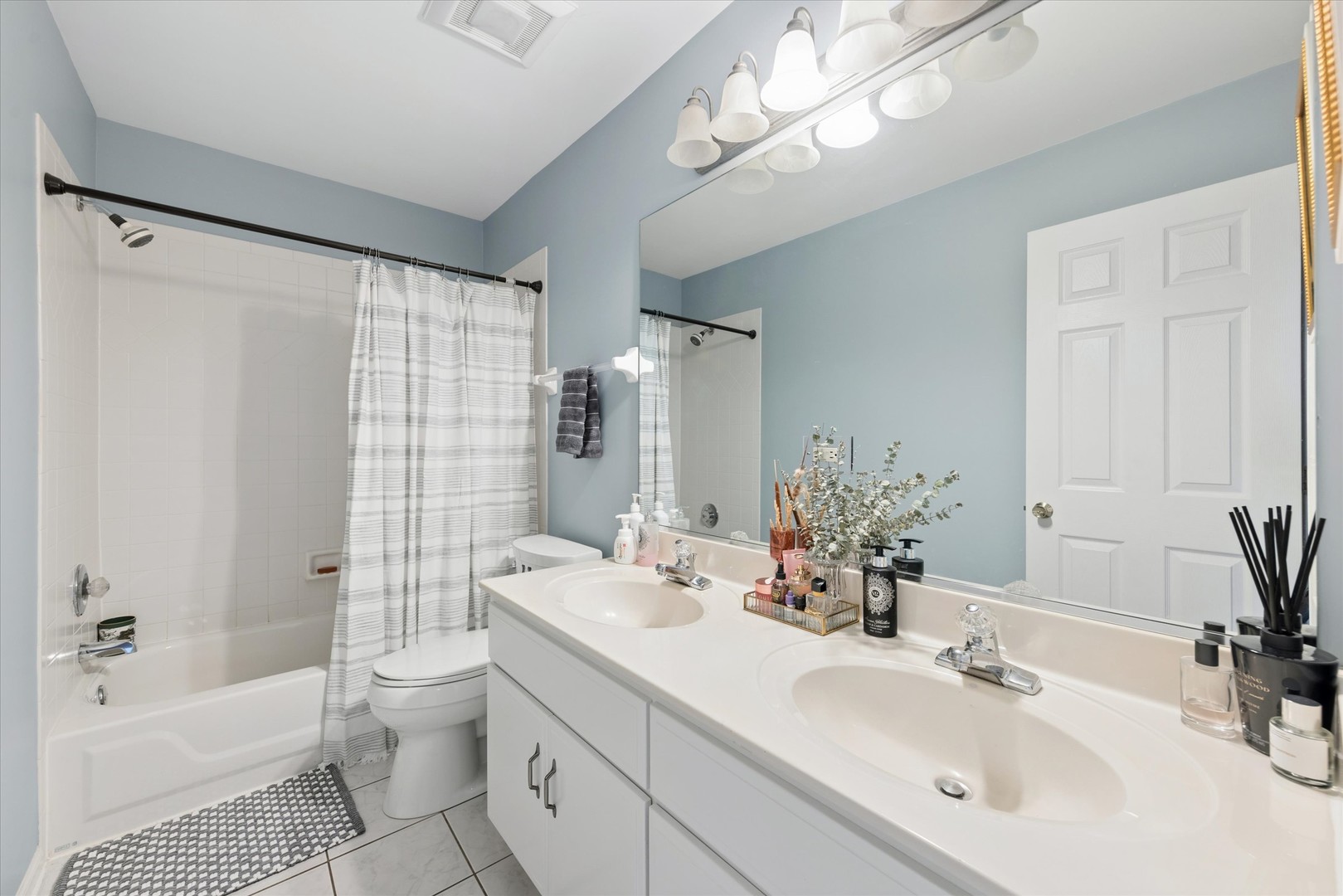 Bathroom with a white double vanity, large mirror, and bathtub with a striped shower curtain.