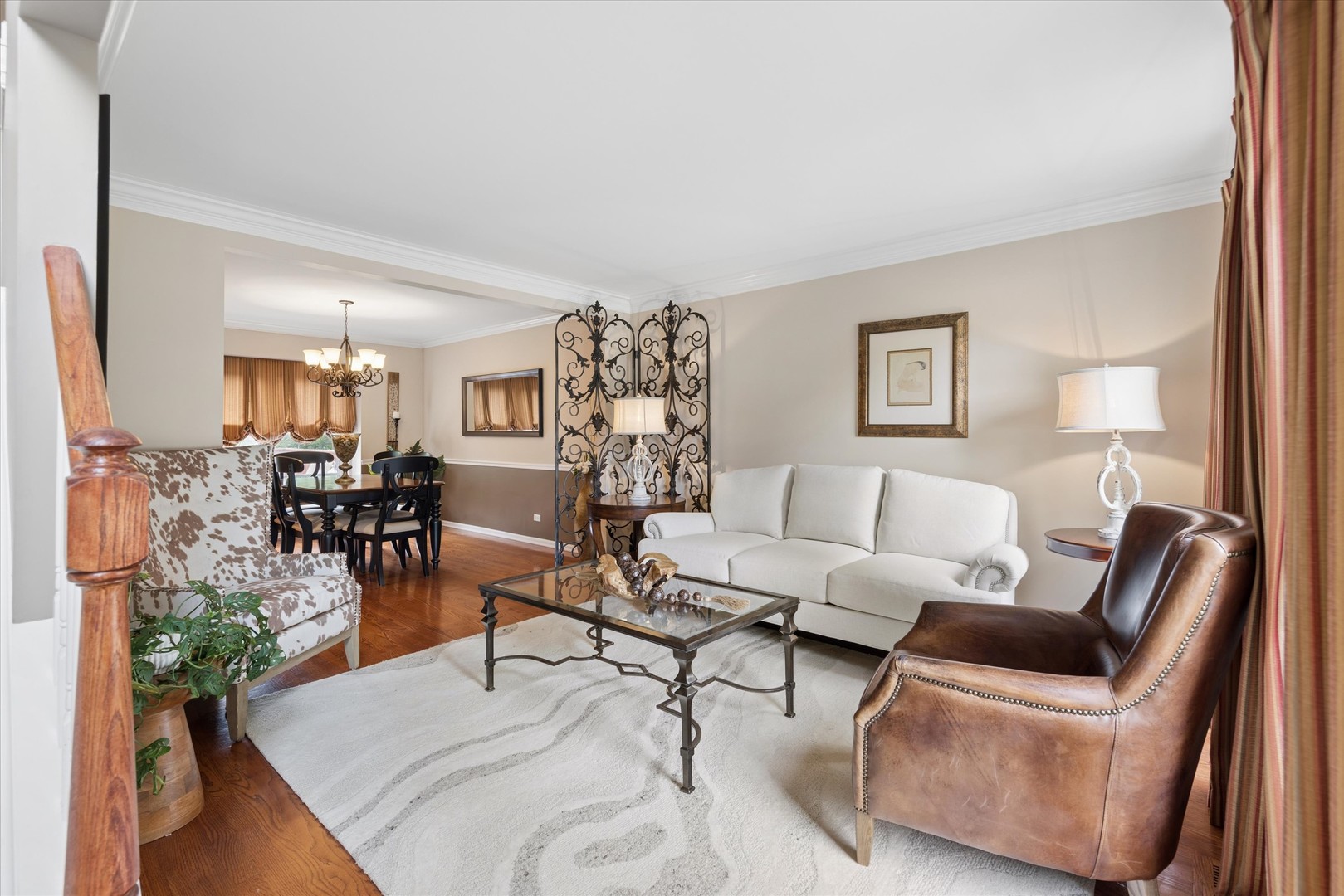 Living room with a white sofa, leather armchair, glass coffee table, and adjoining dining area.