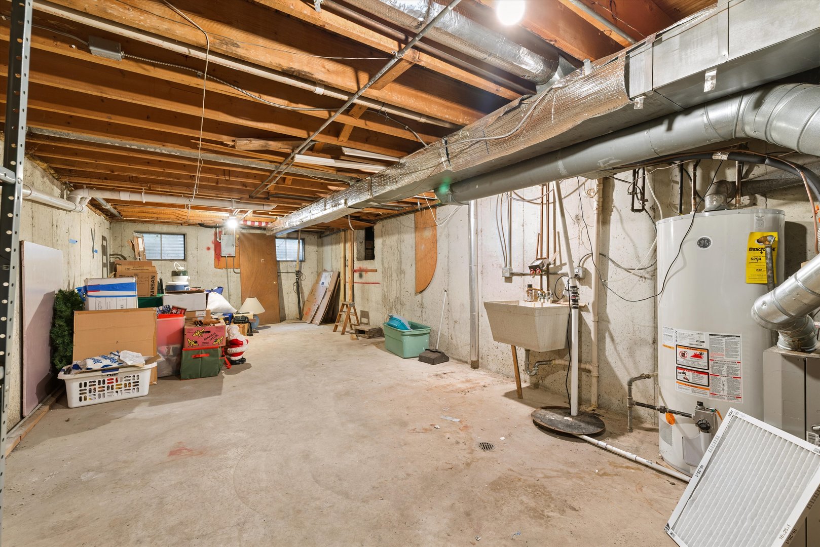 Basement utility room with exposed joists, HVAC ducts, a water heater, and a utility sink.