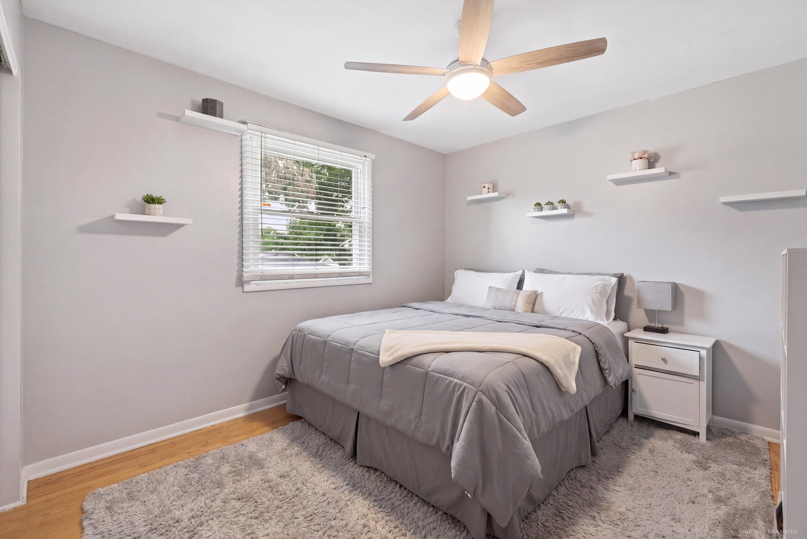Staged bedroom with a gray bed, floating shelves, and a ceiling fan.
