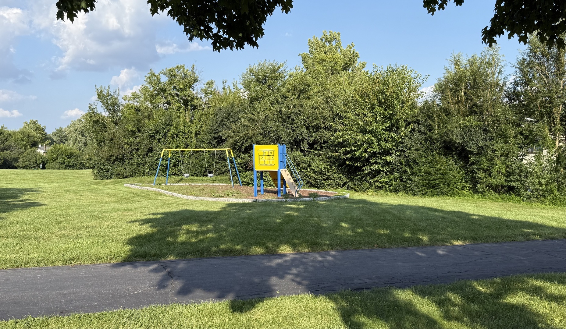 Outdoor playground with swings and a yellow-and-blue slide structure on a grassy lawn.