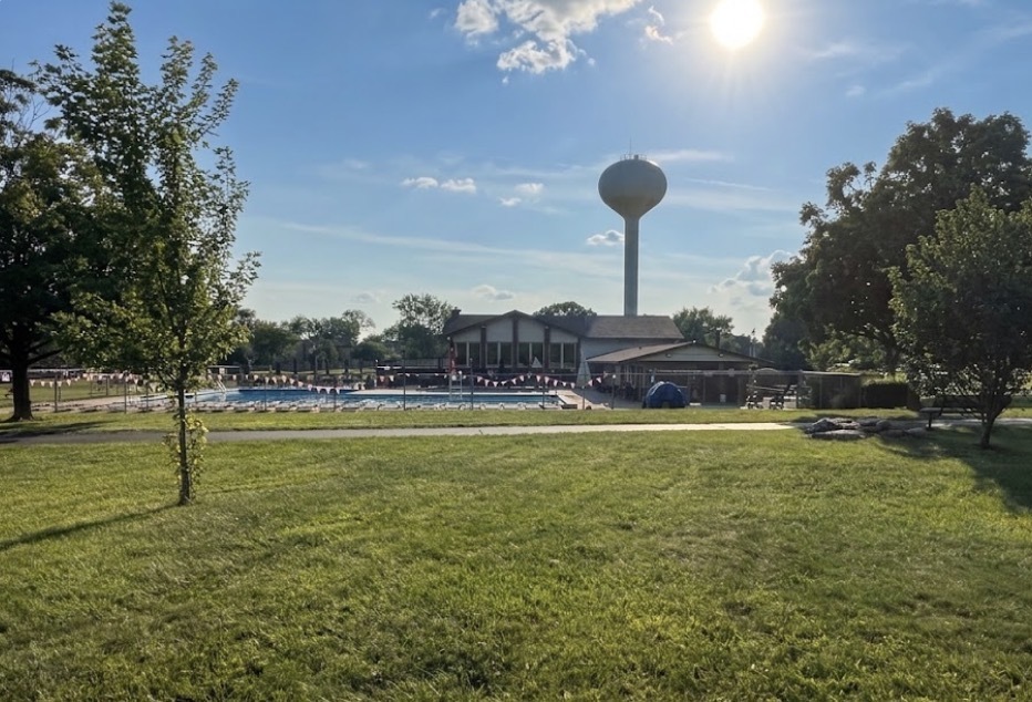 Outdoor pool and clubhouse beyond a grassy lawn, with a water tower in the background.