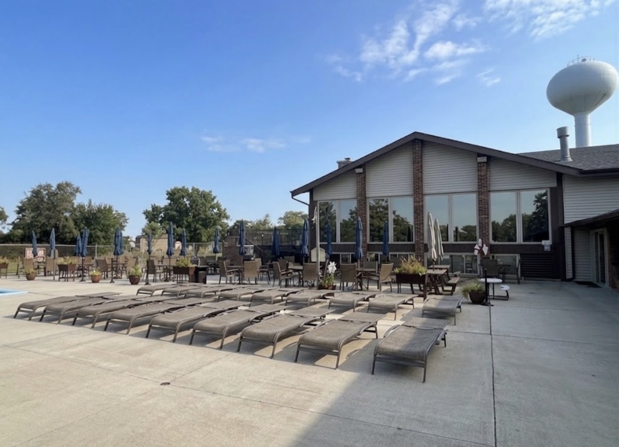 Clubhouse beside a spacious pool deck lined with lounge chairs and closed umbrellas.