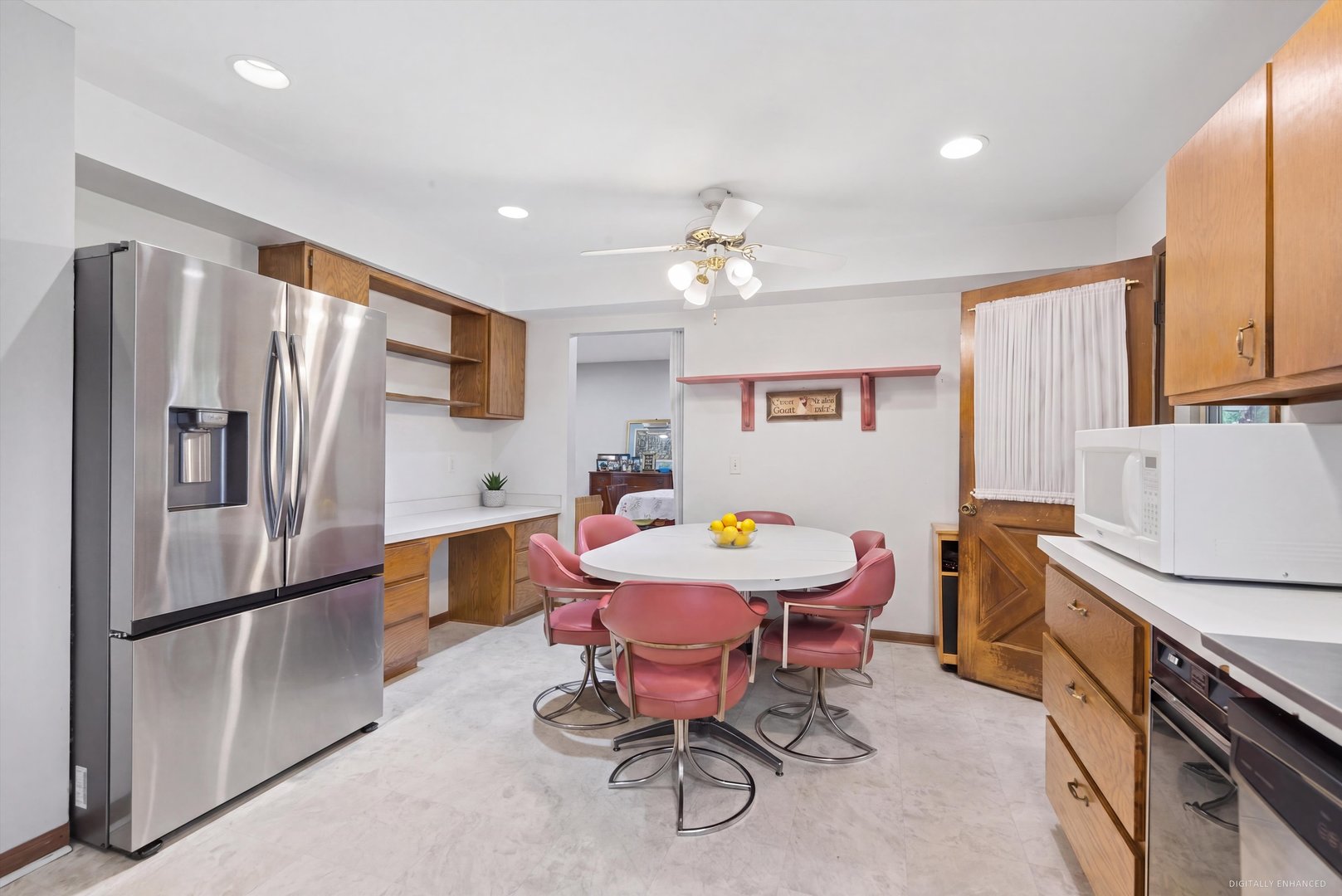 Kitchen with stainless steel refrigerator, wood cabinets, and oval dining table surrounded by red chairs.