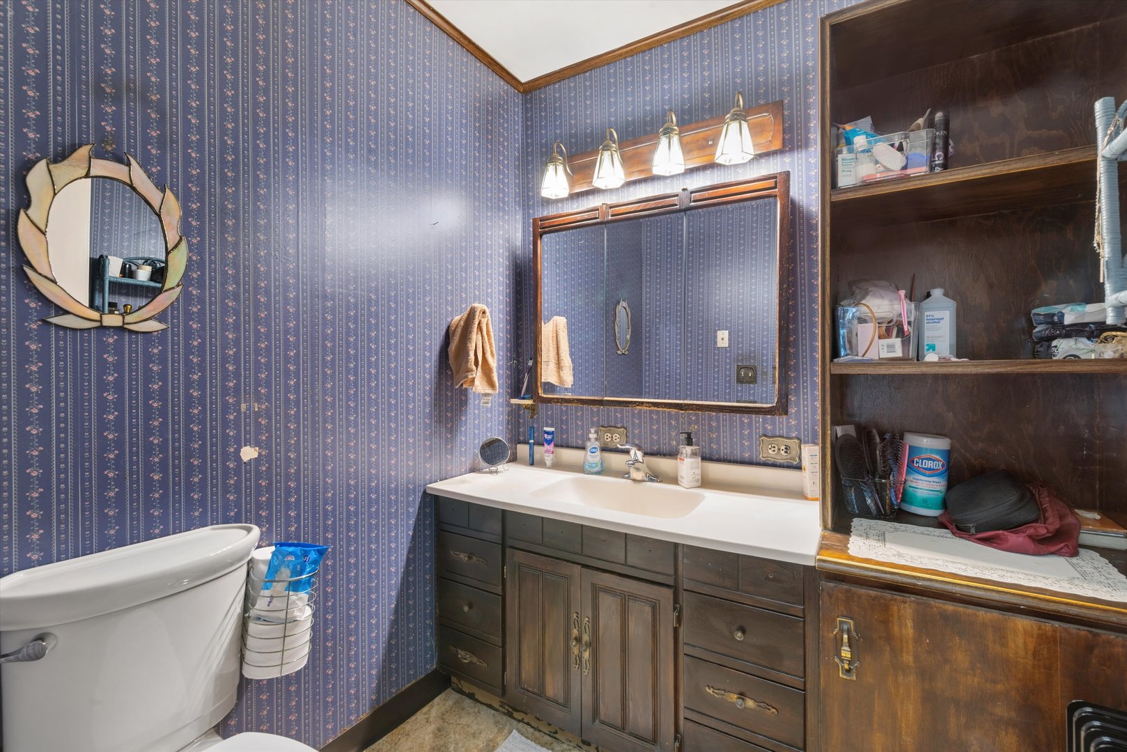 Bathroom with a dark wood vanity, large mirror, blue patterned wallpaper, and built-in shelves.