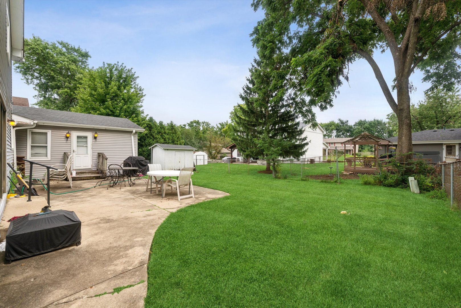 Backyard with a broad lawn, patio seating, storage shed, and mature shade trees.
