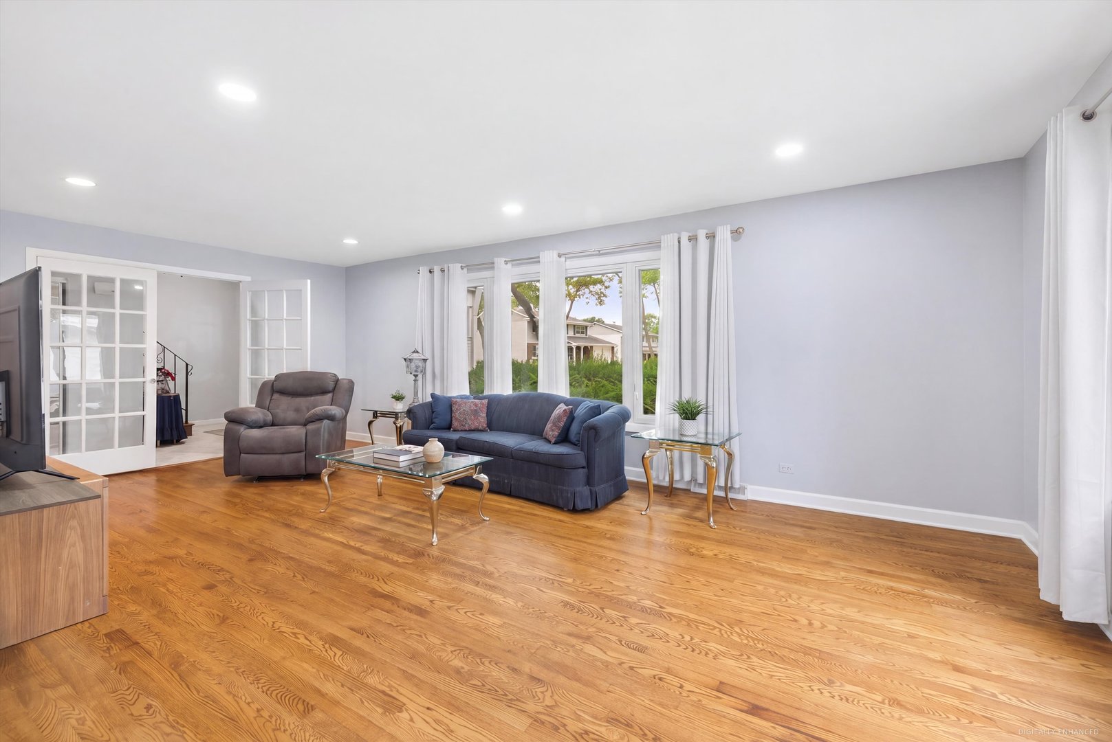 Living room with hardwood floors, blue sofa, gray recliner, and large curtained windows.